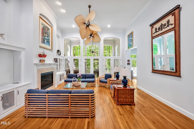 living area featuring a ceiling fan, crown molding, a fireplace, wood finished floors, and baseboards