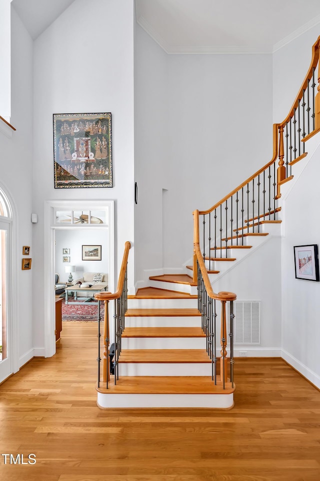 stairs featuring baseboards, a high ceiling, visible vents, and wood finished floors
