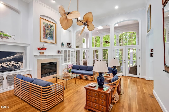 living area with crown molding, a high end fireplace, light wood finished floors, and a towering ceiling