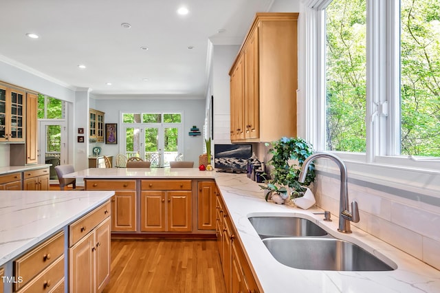 kitchen featuring ornamental molding, a peninsula, light stone countertops, a sink, and light wood finished floors
