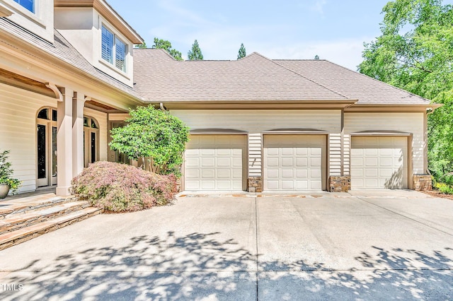 exterior space with an attached garage, a shingled roof, stone siding, and concrete driveway