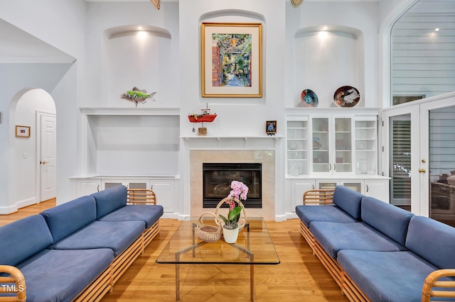 living area featuring ornamental molding, built in features, wood finished floors, a fireplace, and arched walkways