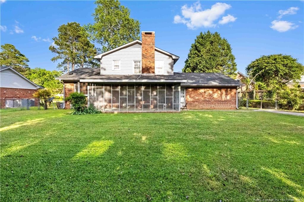 back of property featuring a chimney, a yard, brick siding, and a sunroom