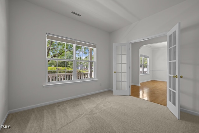 carpeted spare room with french doors, visible vents, arched walkways, vaulted ceiling, and baseboards