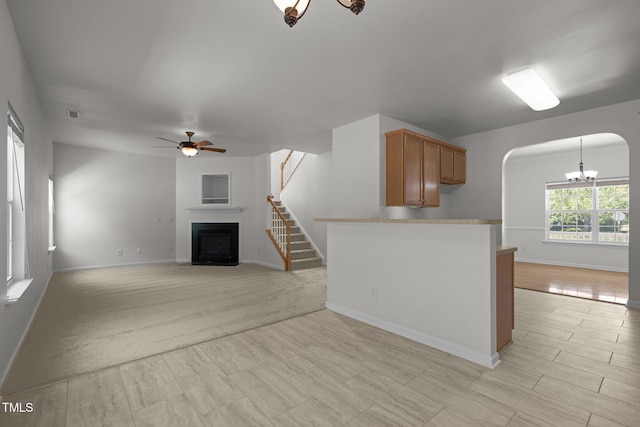unfurnished living room with baseboards, arched walkways, ceiling fan with notable chandelier, and a fireplace