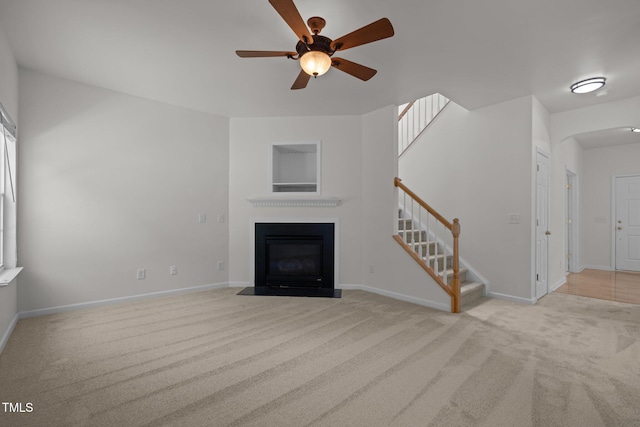 unfurnished living room with a ceiling fan, baseboards, stairway, a fireplace with flush hearth, and carpet