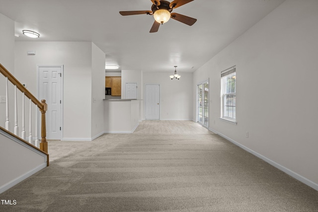 empty room featuring light colored carpet, baseboards, ceiling fan with notable chandelier, and stairs