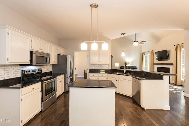 kitchen with appliances with stainless steel finishes, a peninsula, dark countertops, a ceiling fan, and open floor plan