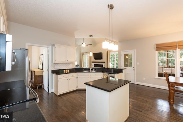 kitchen with a peninsula, dark countertops, dark wood finished floors, a sink, and white cabinetry