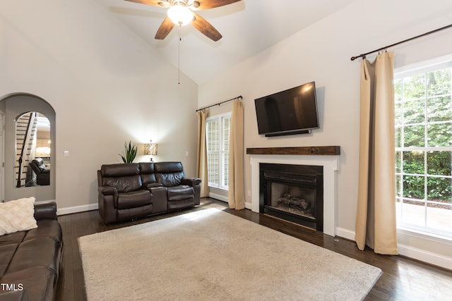 living room featuring a ceiling fan, dark wood-type flooring, a fireplace, arched walkways, and high vaulted ceiling
