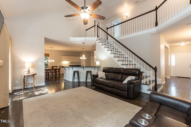 living room with a high ceiling, dark wood-style floors, a ceiling fan, stairway, and baseboards