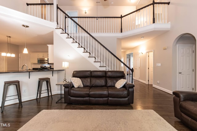 living area with a towering ceiling, dark wood-style flooring, stairway, baseboards, and arched walkways
