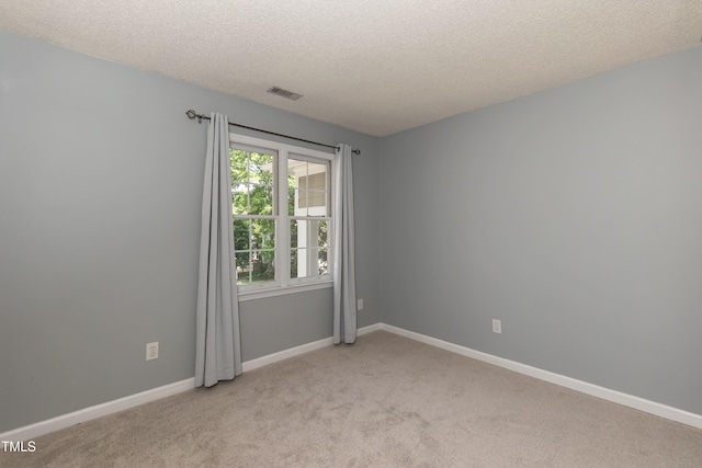 spare room featuring light colored carpet, a textured ceiling, and baseboards