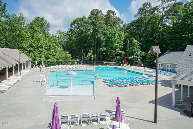 community pool with fence, a patio area, and view of wooded area