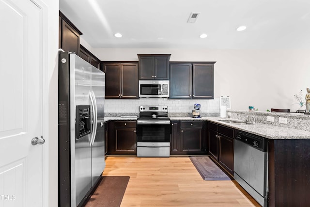 513 Commons Dr, Holly Springs, NC 27540 - kitchen with a peninsula, light wood-type flooring, light stone counters, a sink, and appliances with stainless steel finishes