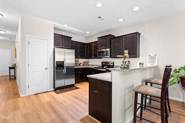 513 Commons Dr, Holly Springs, NC 27540 - kitchen with visible vents, a peninsula, dark brown cabinets, a breakfast bar, and stainless steel appliances