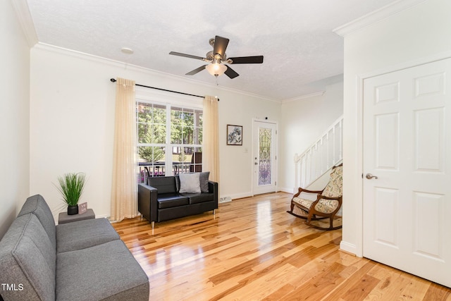 living area with ornamental molding, a textured ceiling, stairway, ceiling fan, and light wood-style flooring