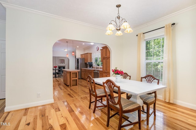 dining area with ornamental molding, light wood-style floors, baseboards, and arched walkways