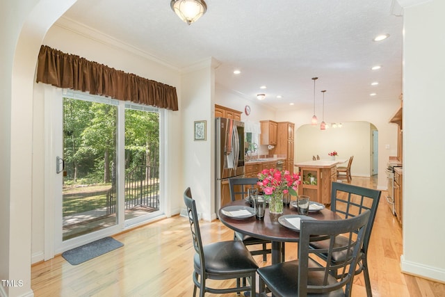 dining room with crown molding, light wood-type flooring, baseboards, arched walkways, and recessed lighting