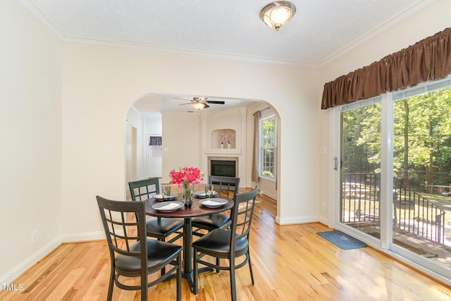 dining room with arched walkways, light wood-type flooring, and a glass covered fireplace