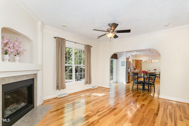 living room with ceiling fan, light wood-style flooring, arched walkways, and visible vents