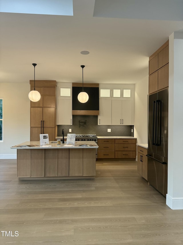 kitchen featuring high end black fridge, light wood-type flooring, decorative backsplash, and baseboards
