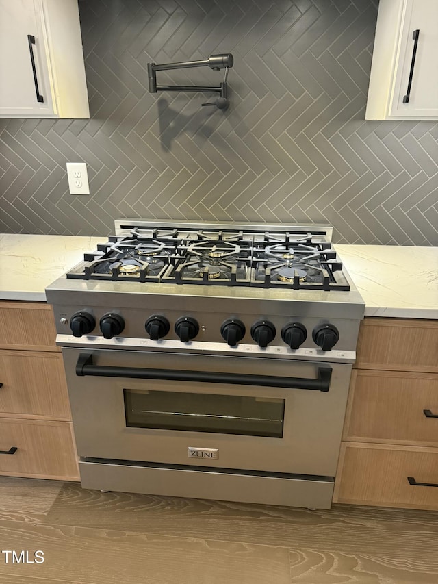 details with light stone counters, backsplash, white cabinets, and high end stainless steel range