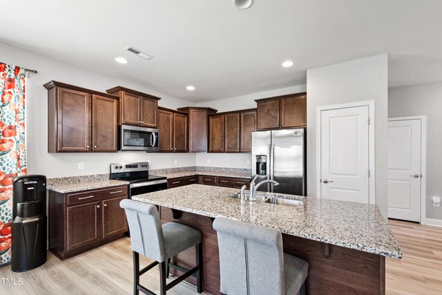 147 Antler Steel Dr, Clayton, NC 27527 - kitchen featuring light stone countertops, dark brown cabinetry, appliances with stainless steel finishes, a sink, and light wood-type flooring