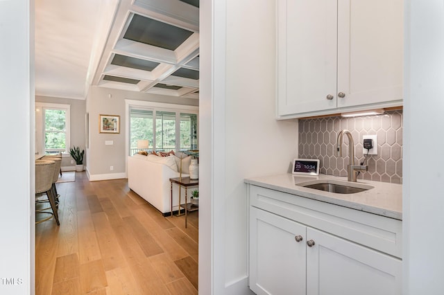 bar featuring baseboards, light wood-style flooring, a sink, coffered ceiling, and backsplash