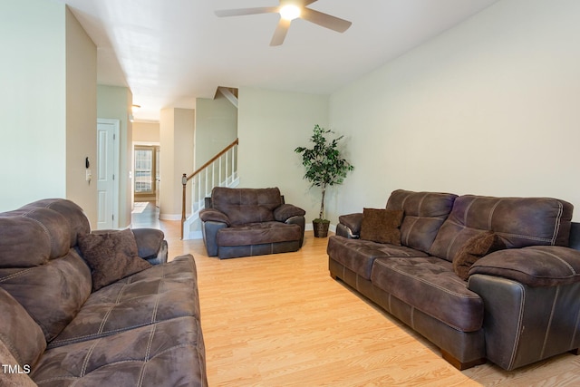 living room featuring baseboards, a ceiling fan, light wood finished floors, and stairway