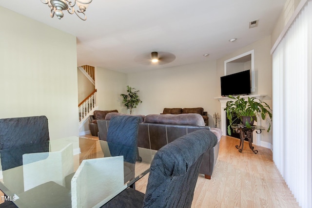 living room with visible vents, light wood-type flooring, baseboards, ceiling fan with notable chandelier, and stairs