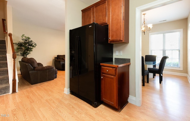 kitchen with brown cabinets, light wood-type flooring, black refrigerator with ice dispenser, and a notable chandelier