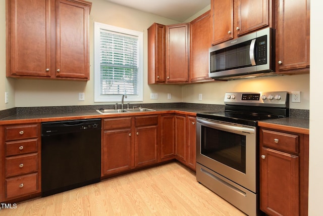 kitchen with dark countertops, brown cabinets, light wood-type flooring, a sink, and stainless steel appliances