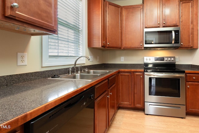 kitchen with brown cabinetry, dark countertops, a sink, stainless steel appliances, and light wood-style flooring
