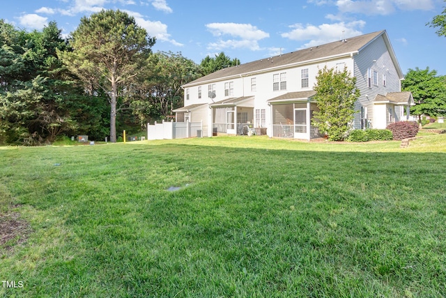 rear view of property featuring a sunroom, roof with shingles, fence, and a yard