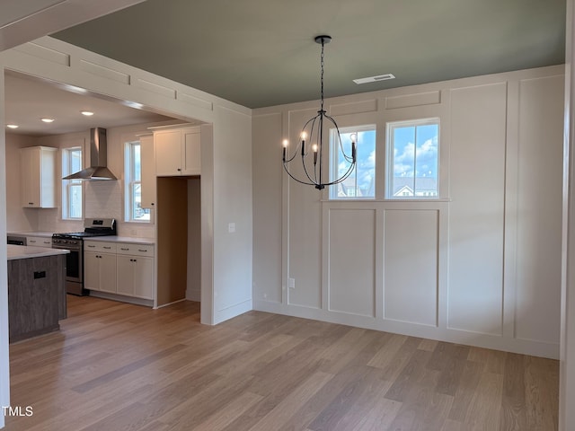 1720 Bright Lantern Way, Wendell, NC 27591 - kitchen featuring stainless steel range with gas cooktop, wall chimney exhaust hood, light wood-type flooring, a chandelier, and light countertops