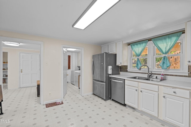 kitchen featuring light floors, a sink, white cabinetry, stainless steel appliances, and separate washer and dryer