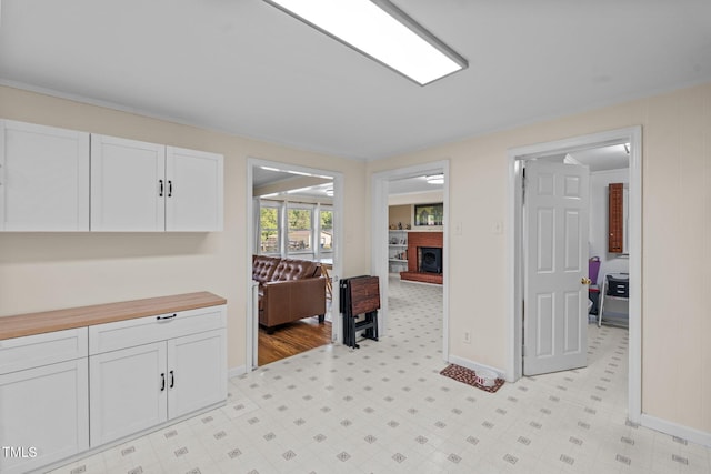 kitchen featuring white cabinetry, light floors, a brick fireplace, and baseboards