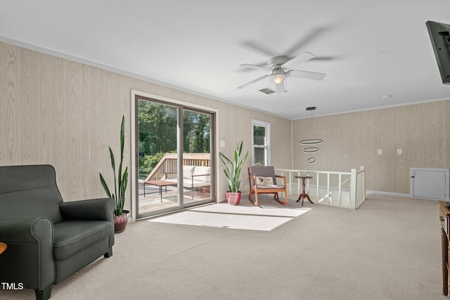 living area featuring a ceiling fan, carpet, visible vents, crown molding, and an upstairs landing