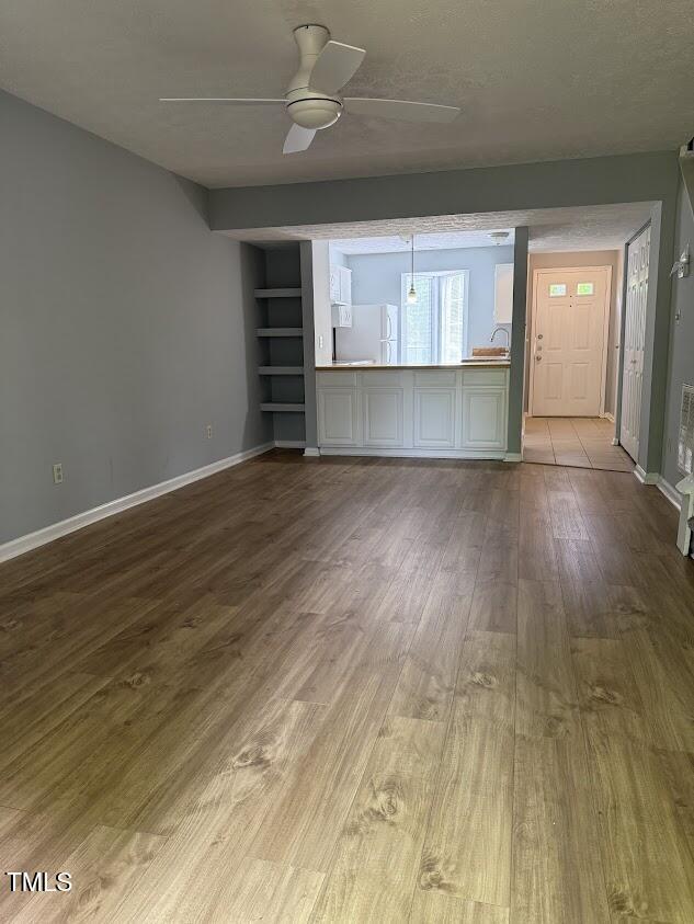 unfurnished living room with dark wood-type flooring, baseboards, ceiling fan, and built in features