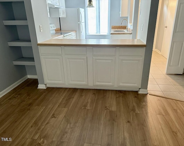 interior space with a sink, white appliances, exhaust hood, light countertops, and white cabinets