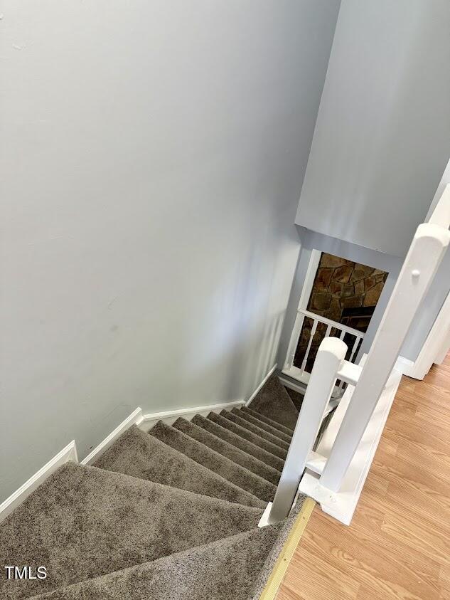stairway featuring wood finished floors, baseboards, and a stone fireplace