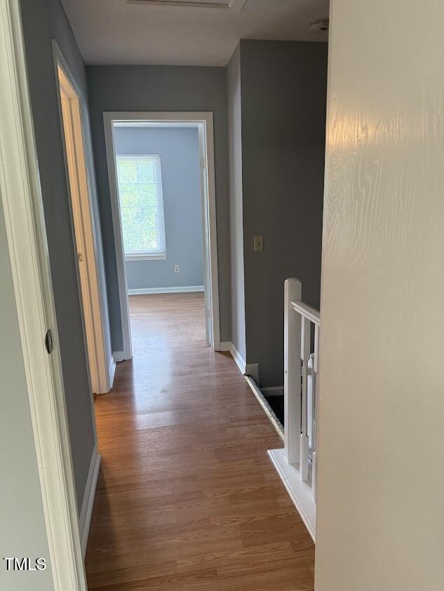 hall with an upstairs landing, wood finished floors, and baseboards