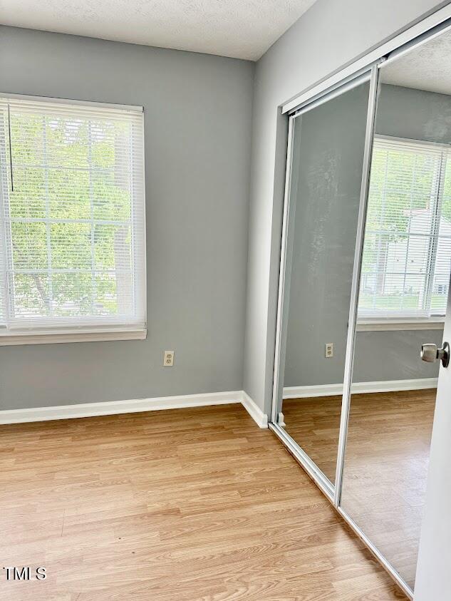 unfurnished bedroom with baseboards, multiple windows, light wood-style floors, and a closet