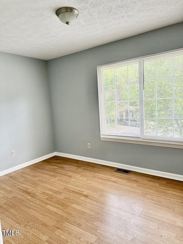 empty room with baseboards, light wood-style floors, visible vents, and a textured ceiling