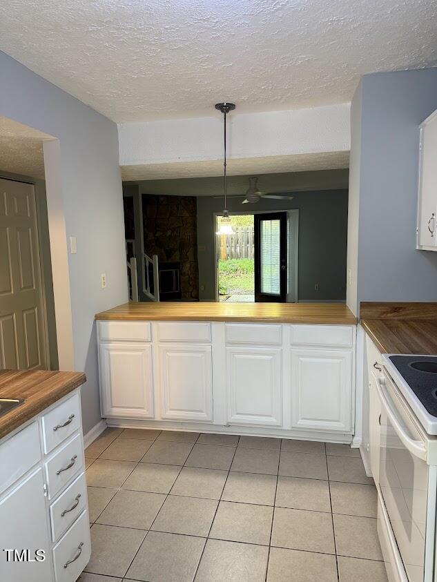 kitchen with wood counters, white electric range oven, light tile patterned floors, and a textured ceiling