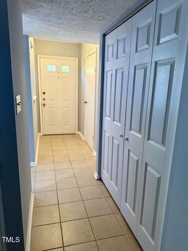 doorway with a textured ceiling, baseboards, and light tile patterned floors