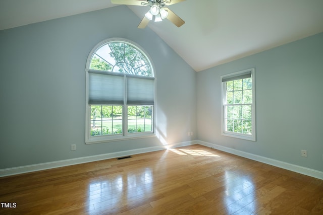 empty room with visible vents, wood finished floors, a healthy amount of sunlight, and vaulted ceiling