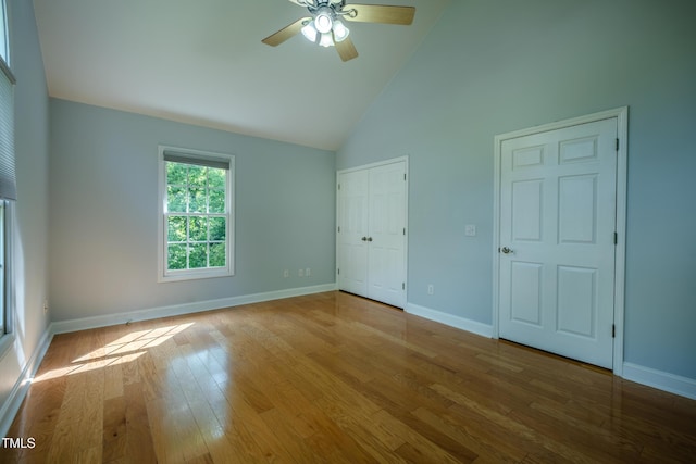 unfurnished bedroom featuring high vaulted ceiling, baseboards, and wood finished floors