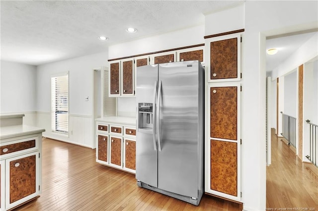 kitchen with light wood-type flooring, a wainscoted wall, stainless steel refrigerator with ice dispenser, and light countertops